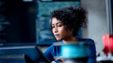Female software developer coding in Python programming language in an open place office space, with screen featuring code blurred in background.
