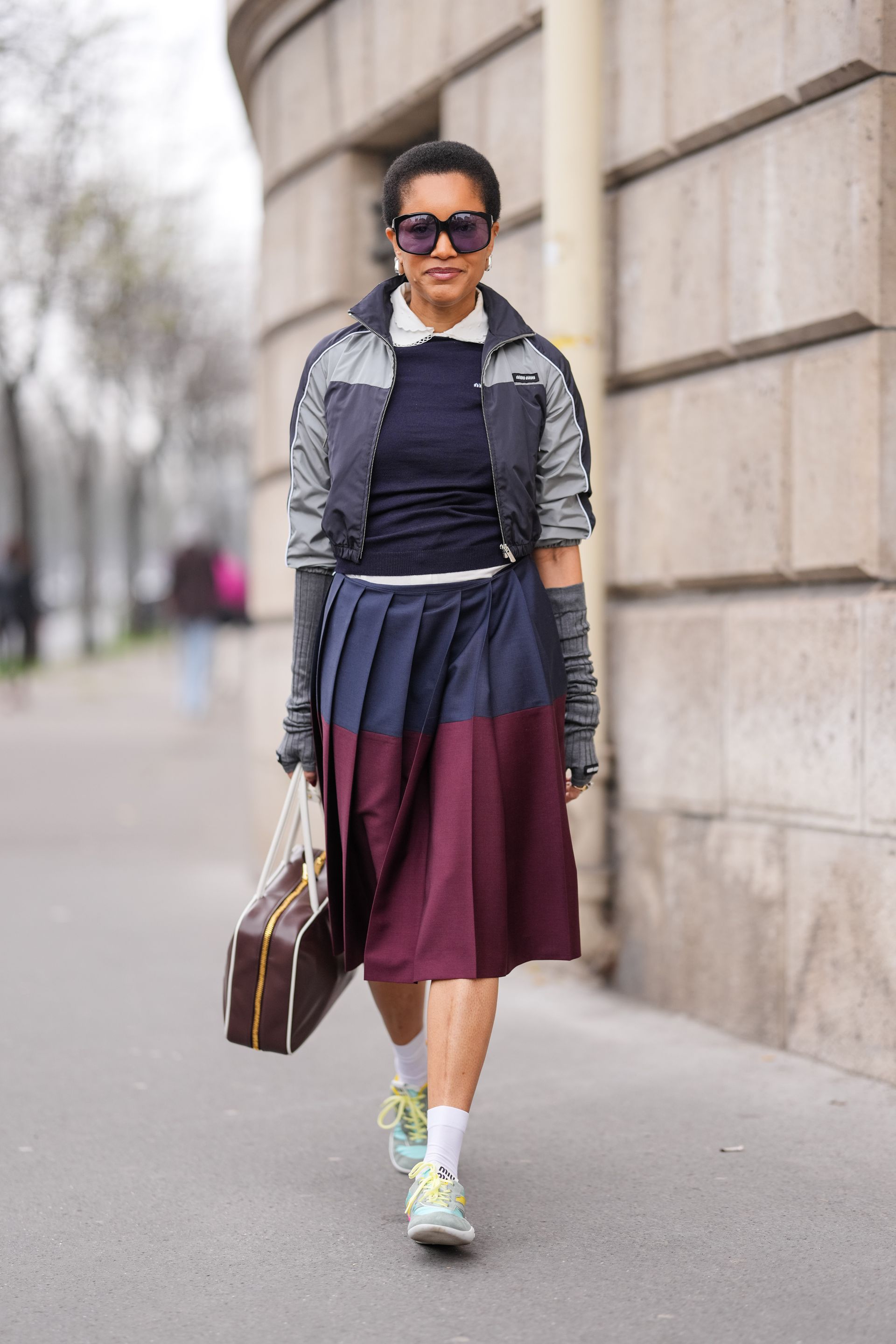 Woman in track jacket and pleated skirt.