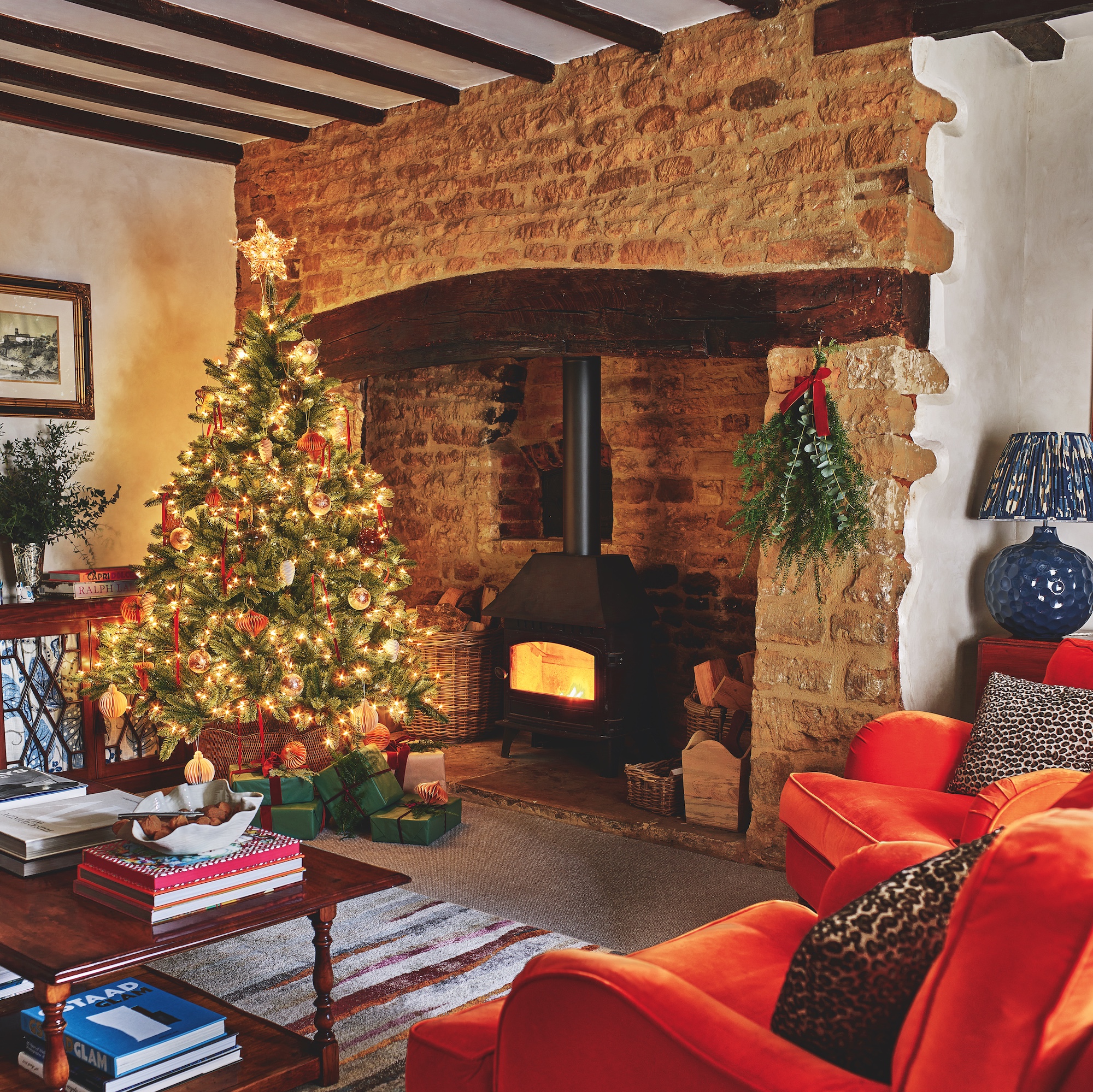 living room with inglenook fireplace with woodburner, beamed ceiling, orange velvet armchairs and christmas tree with lights