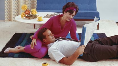 1960s photo of young couple looking at blueprint in living room, smiling