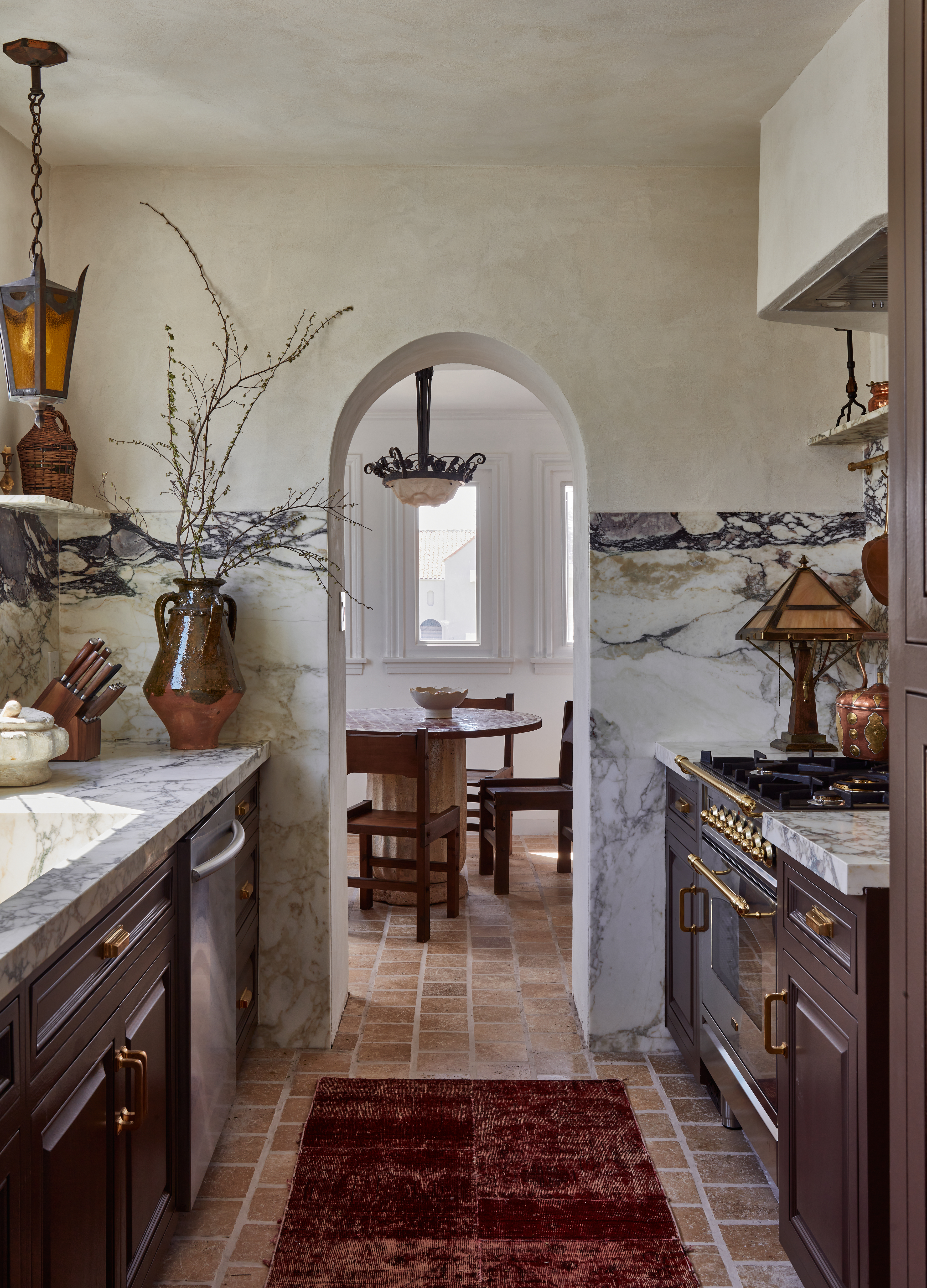 A kitchen with terracotta floor tiles, veined marble countertops and even walls