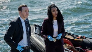Detectives Danny Reagan (Donnie Wahlberg) and Lena Silver (Sonequa Martin-Green) look serious in smart suits while investigating a homicide by the sparking waters of Boston Harbor in spin-off series "Boston Blue".