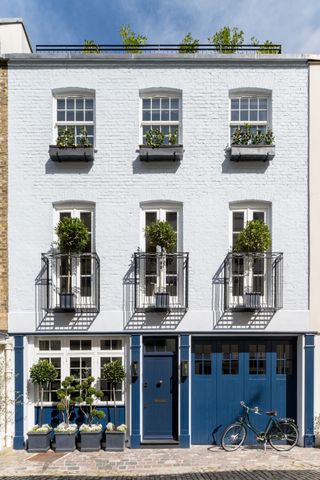A Georgian terrace house with a white brick facade and blue cladding on the ground floor. A bike rests against the house