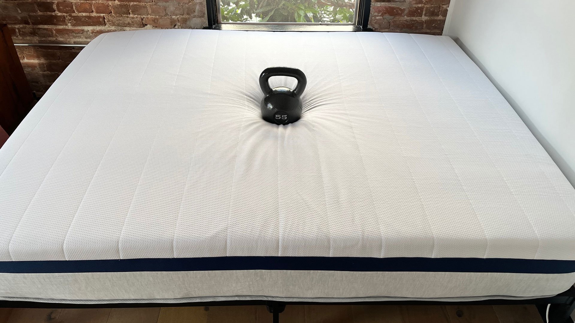 Photo of Helix Midnight mattress in a bedroom, with a weight on it, and a wine glass stood upright on the mattress surface nearby