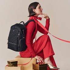 Woman sitting on top of gold parcels in red outfit with black backpack