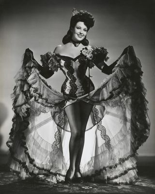 a woman wearing a corseted dress smiles as she holds up her can can like skirt in a promotional still for the movie Hangover Square