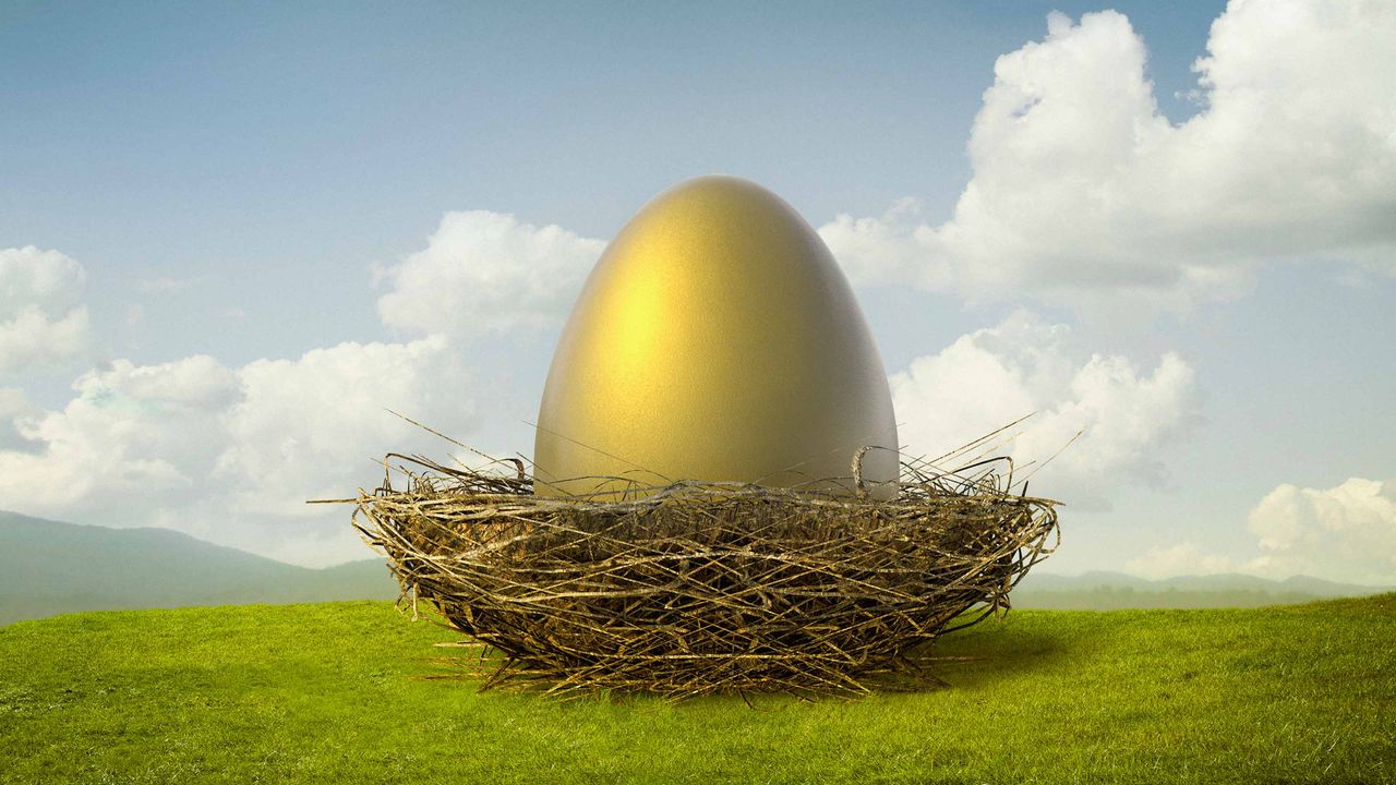 A huge golden egg sits in a bird&amp;#039;s nest on a green hill under a blue sky.