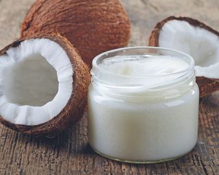 A jar of coconut oil next to coconuts on a wooden table