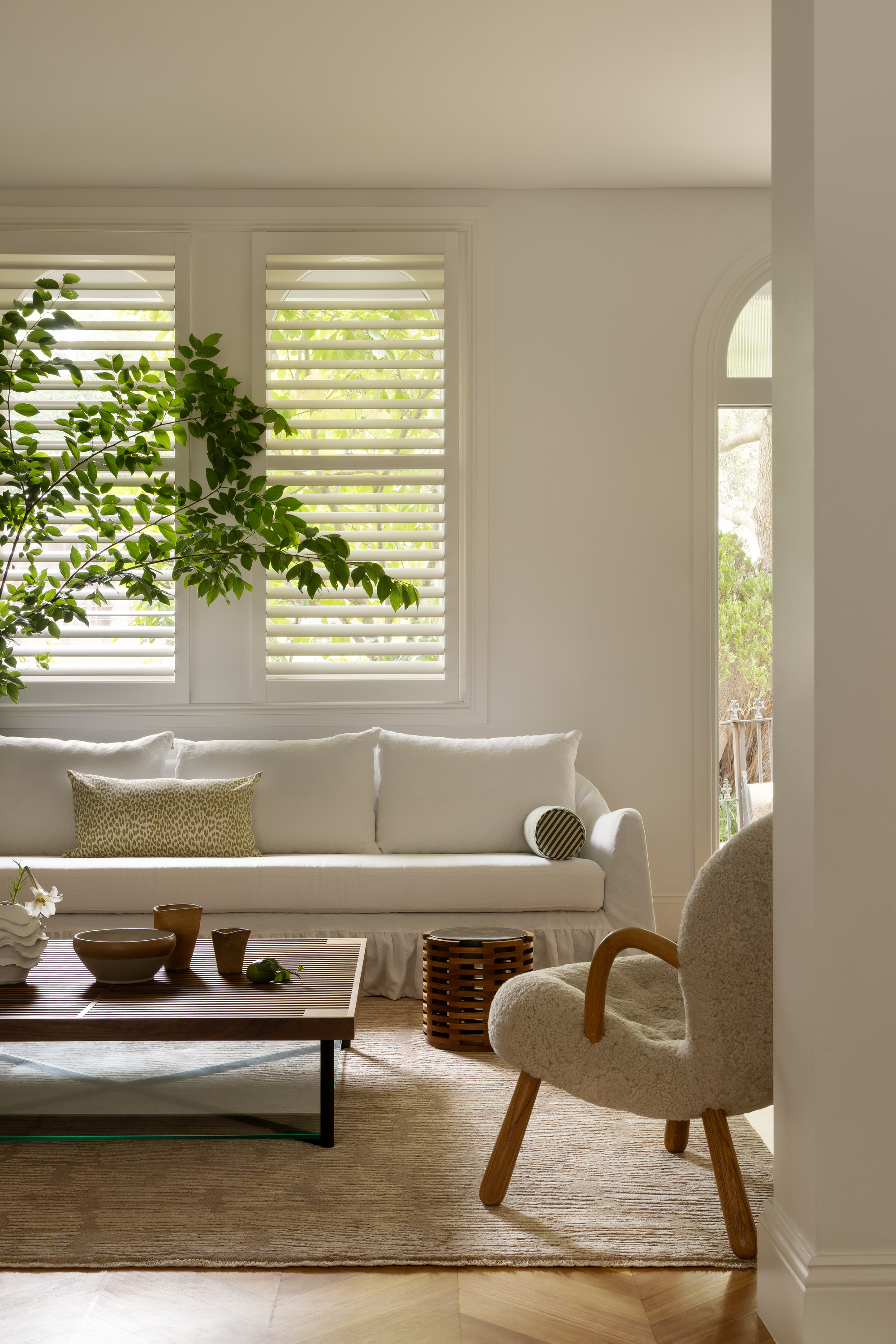 Image of a bright, white living room with a white sofa that has a ruffled skirt, a tan rug, a wooden coffee table, and a boucle accent chair.