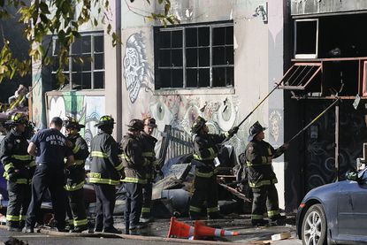 Firefighters work to clear the debris from a doorway following a fire that killed at least nine people at a warehouse in Oakland