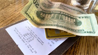 A cash tip and a credit card on top of a dinner bill