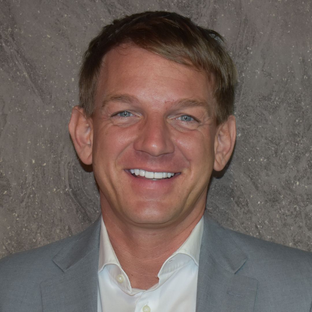 A smiling man with brown hair in a grey suit and white shirt