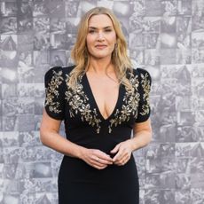 Kate Winslet wearing a loose wave hairstyle. She is wearing a black dress with ornate detailing around the plunging neckline.