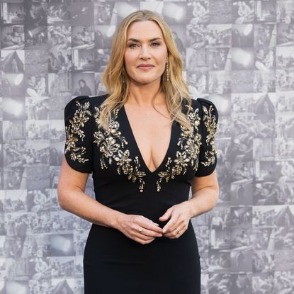 Kate Winslet wearing a loose wave hairstyle. She is wearing a black dress with ornate detailing around the plunging neckline. 