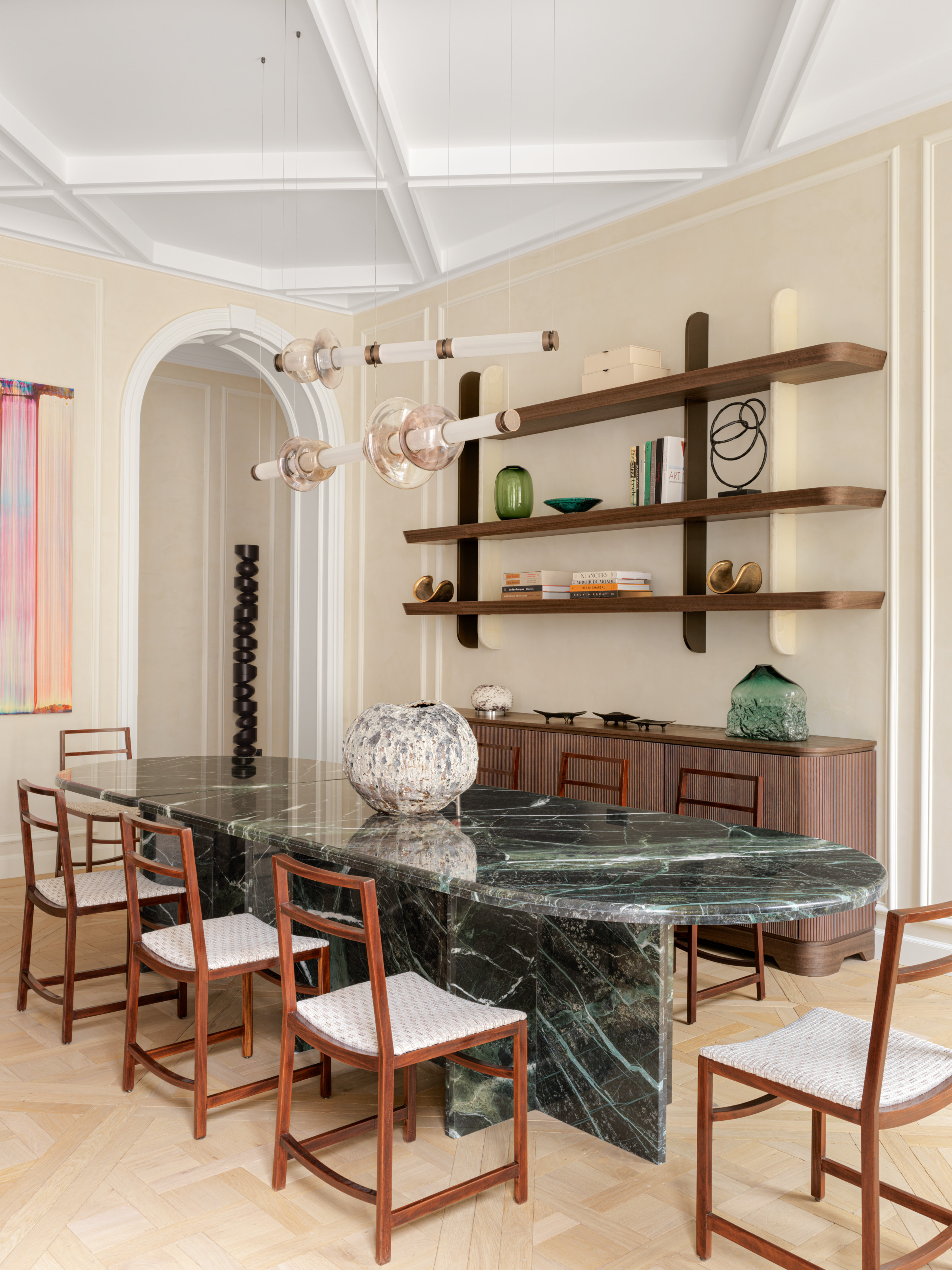 Cream dining room with green marble oval dining table, open shelving above a sideboard, and wooden chairs