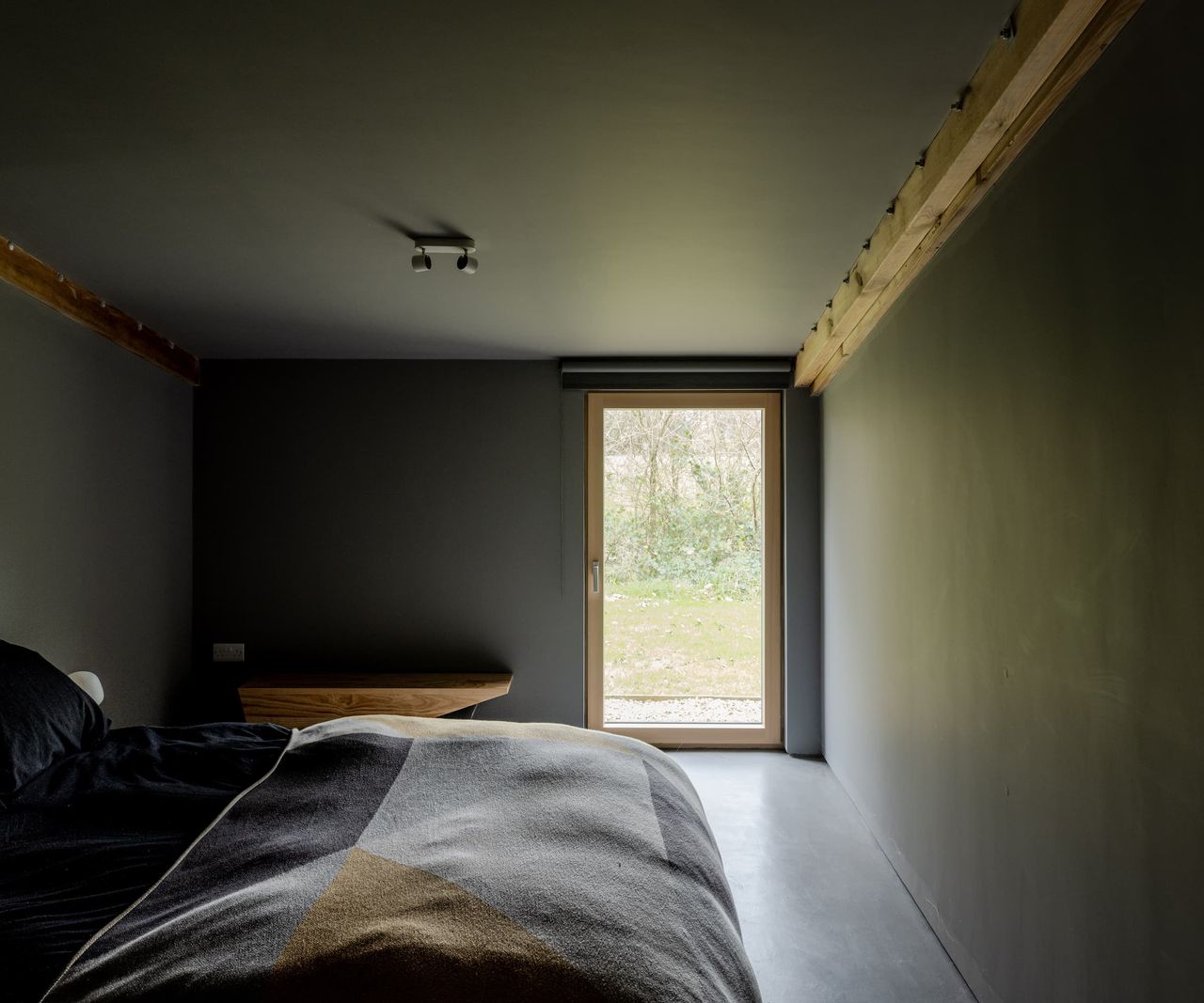 A black bedroom with a door leading to the outside and a side table made of wood