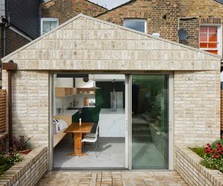 Simple pitched single storey light brick rear extension with large aluminium framed patio doors