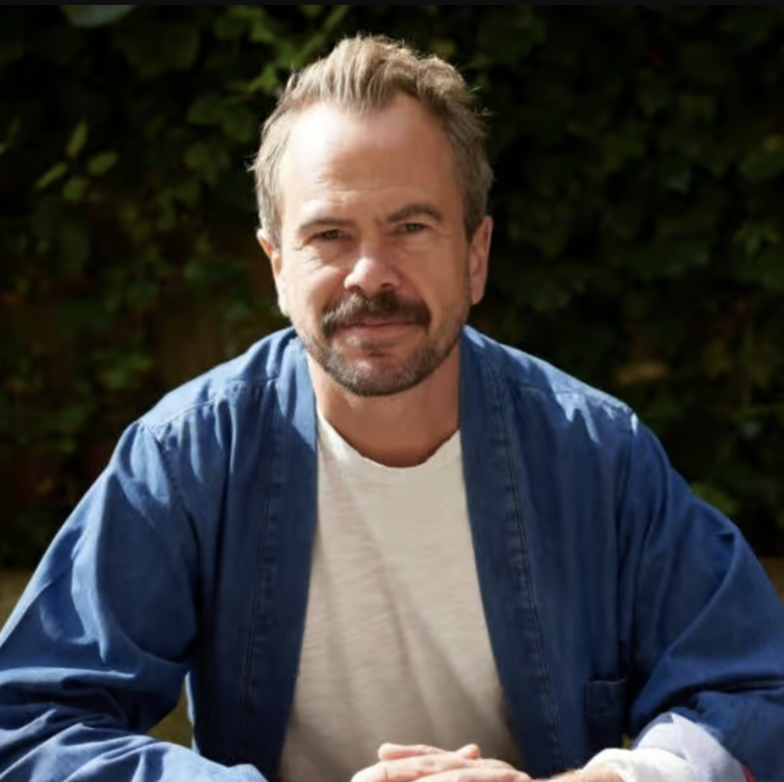 A headshot of a man wearing a blue overshirt