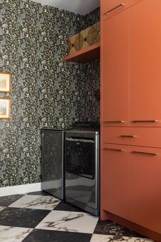 A laundry room with bold wallpaper and orange cabinets