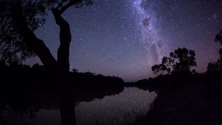 a purple tinted sky illuminated by the stars of the milky way are reflected in the river below.