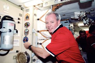 STS-92 commander Brian Duffy adds the patch for the 100th space shuttle mission to the International Space Station's wall in 2000.