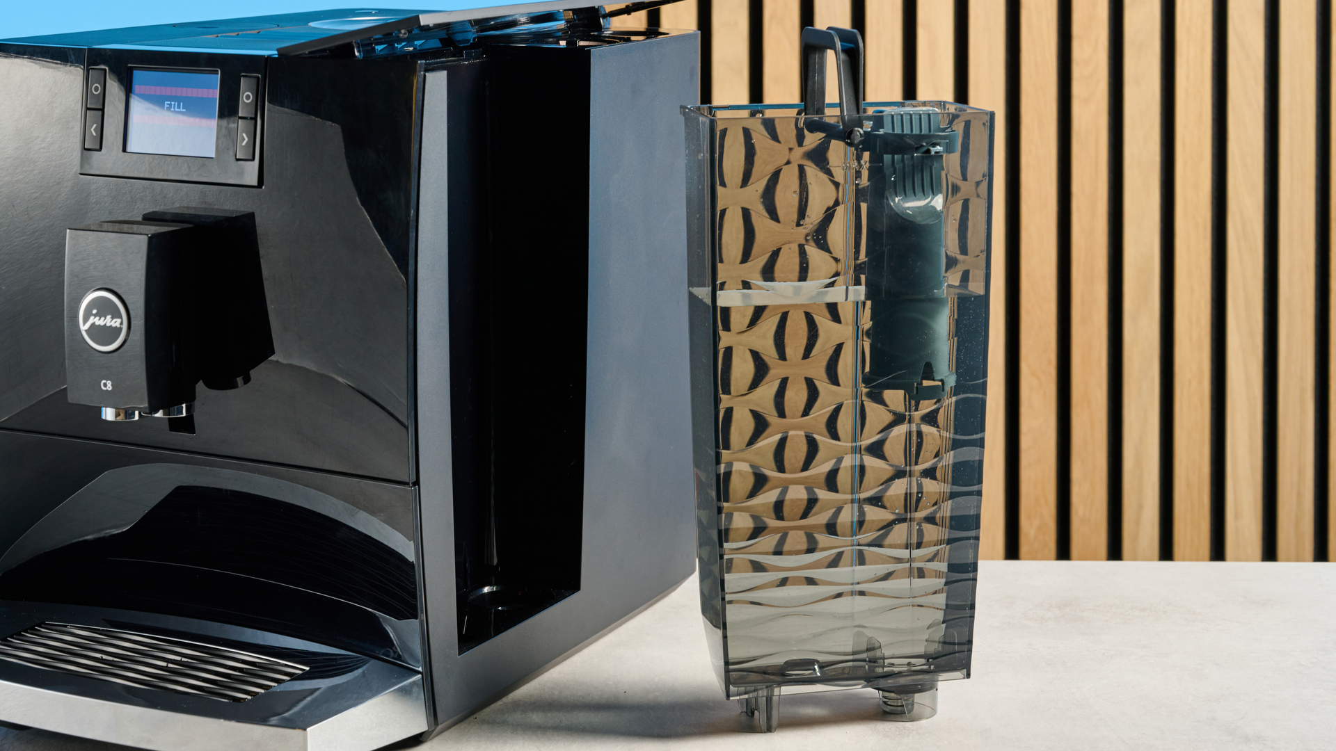 the jura c8 automatic coffee machine in piano black photographed with a blue and wood background