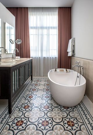 Bathroom with oval bathtub on patterned tiles with freestanding basin cabinets with 2 seperate mirrors