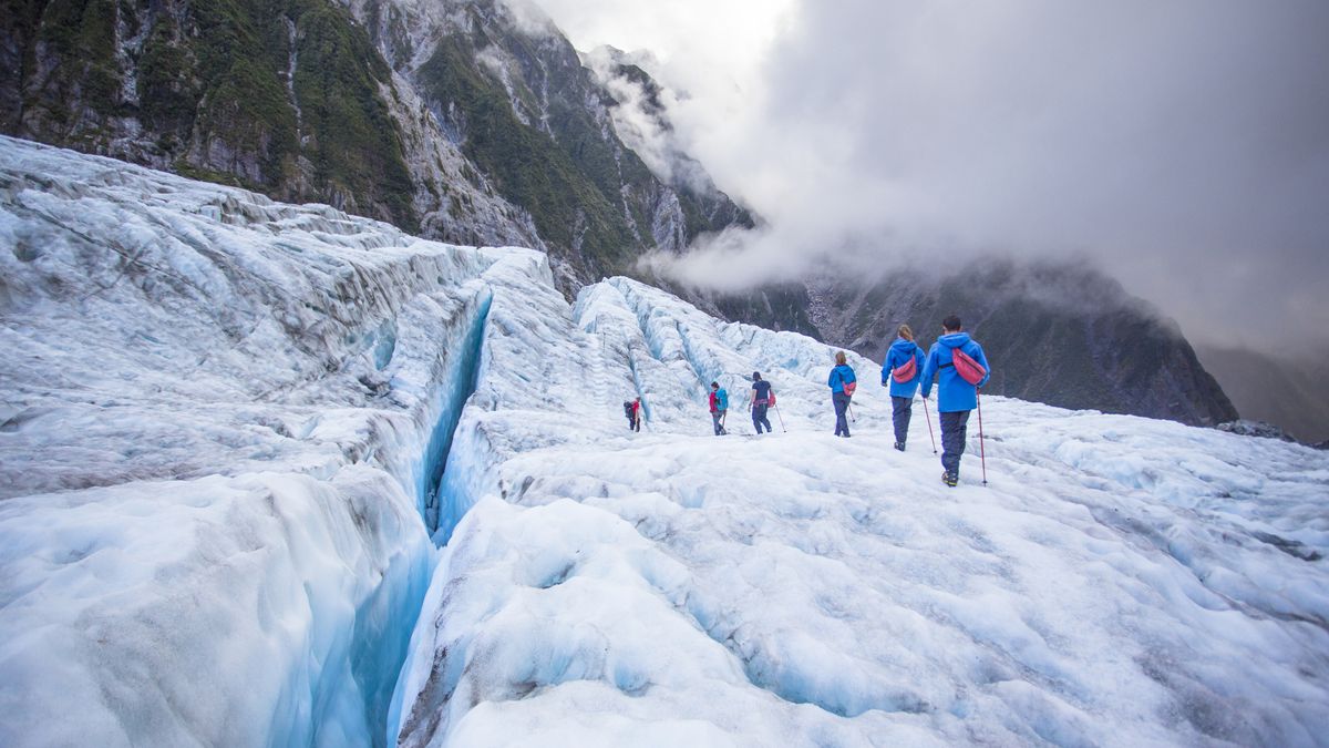 A group crosses a glacier while roped together