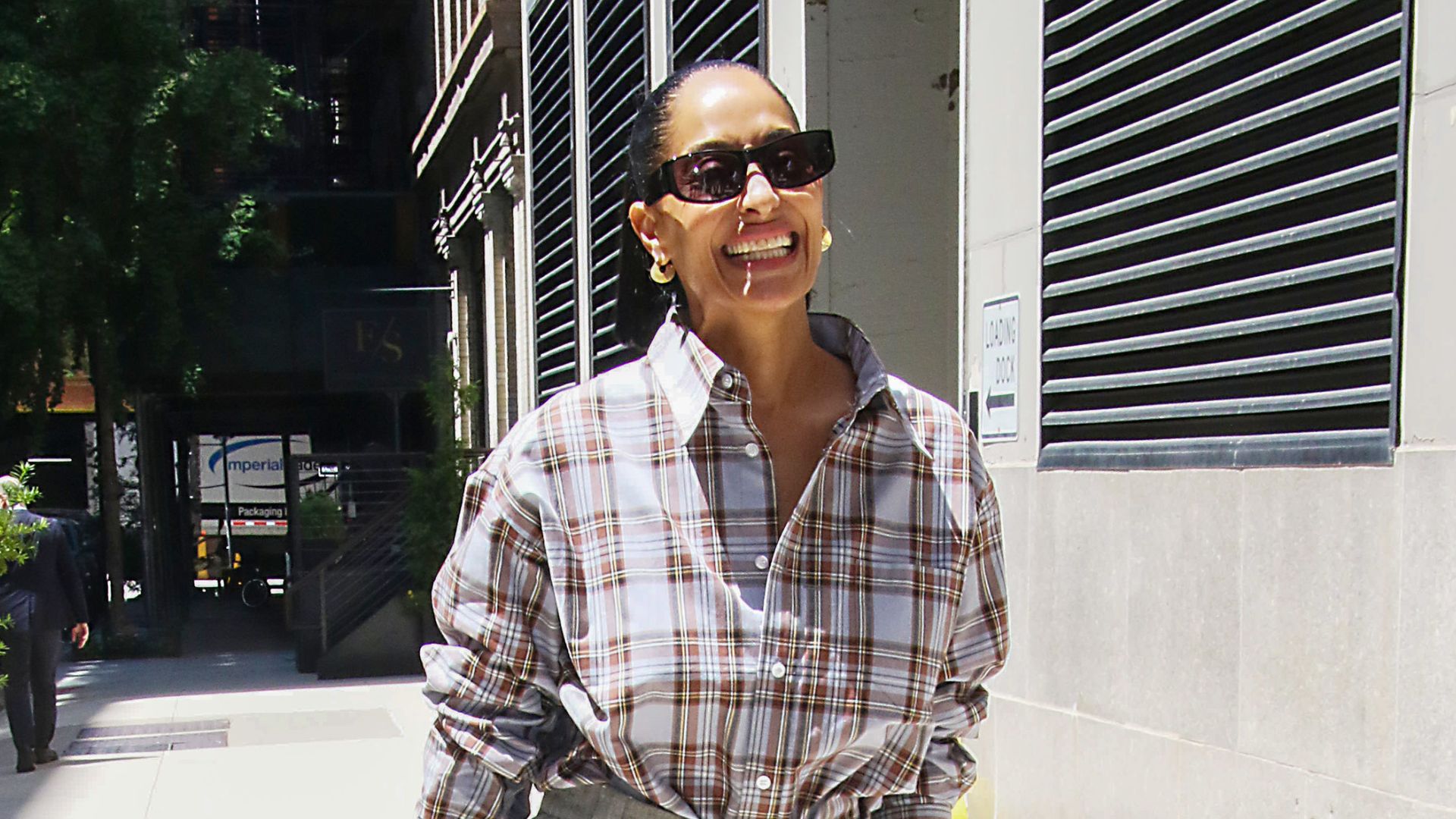 Tracee Ellis Ross wears Bermuda shorts with brown peep-toe mules and a checked shirt.
