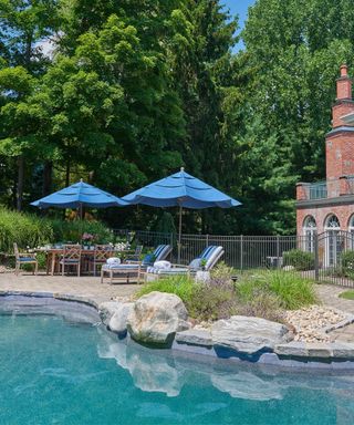 Old money coastal style pool-side patio with blue and white striped sun loungers, blue parasols, and an aged garden dining set