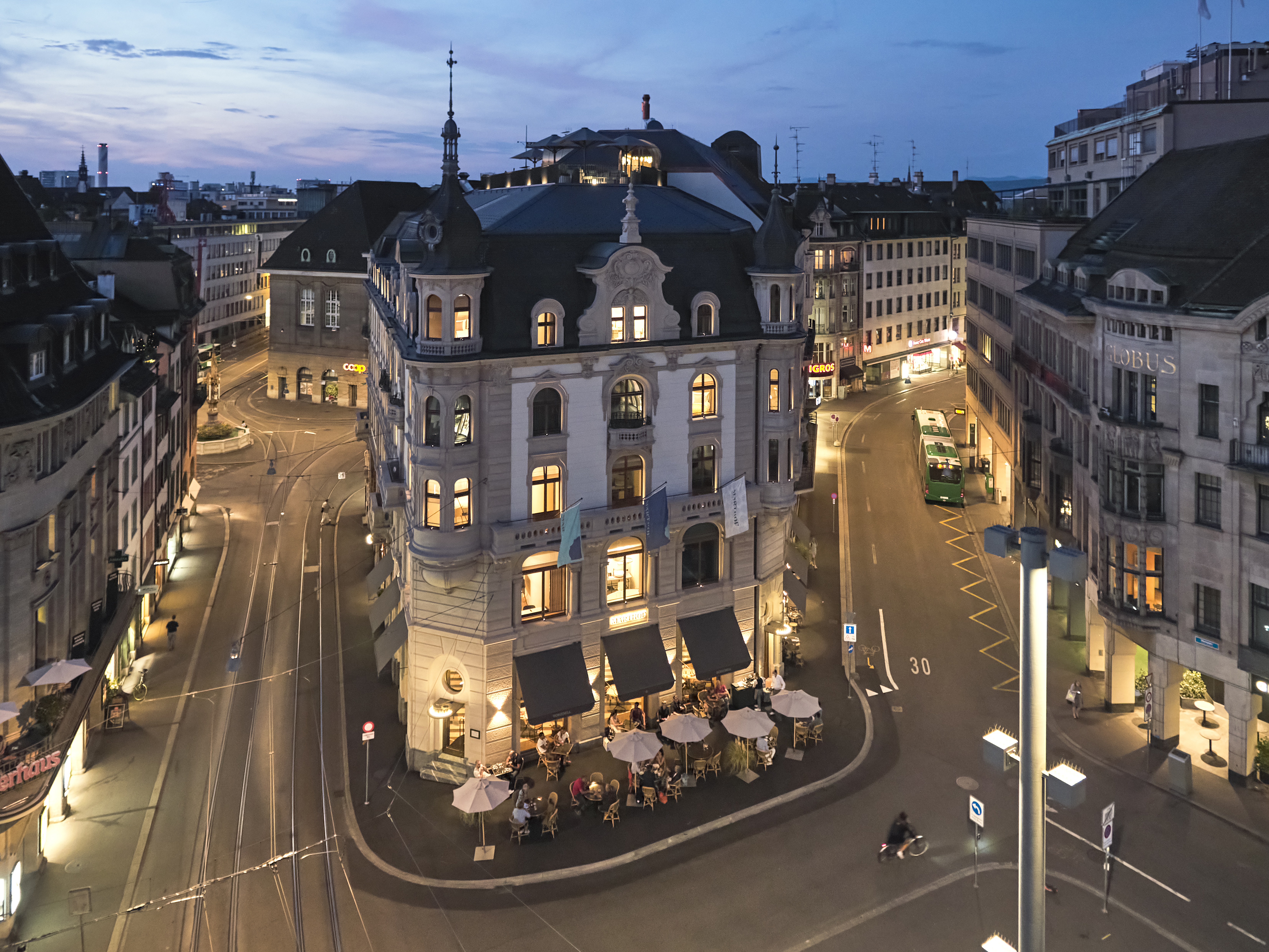 Photos of the exterior of Hotel M&amp;auml;rthof Basel, based in a beautiful square with historical landmarks with umbrella-covered tables dining at the bar outside
