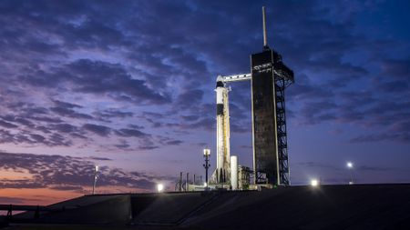 A white and black SpaecX rocket with NASA and SpaceX logos on the side atop a launch pad