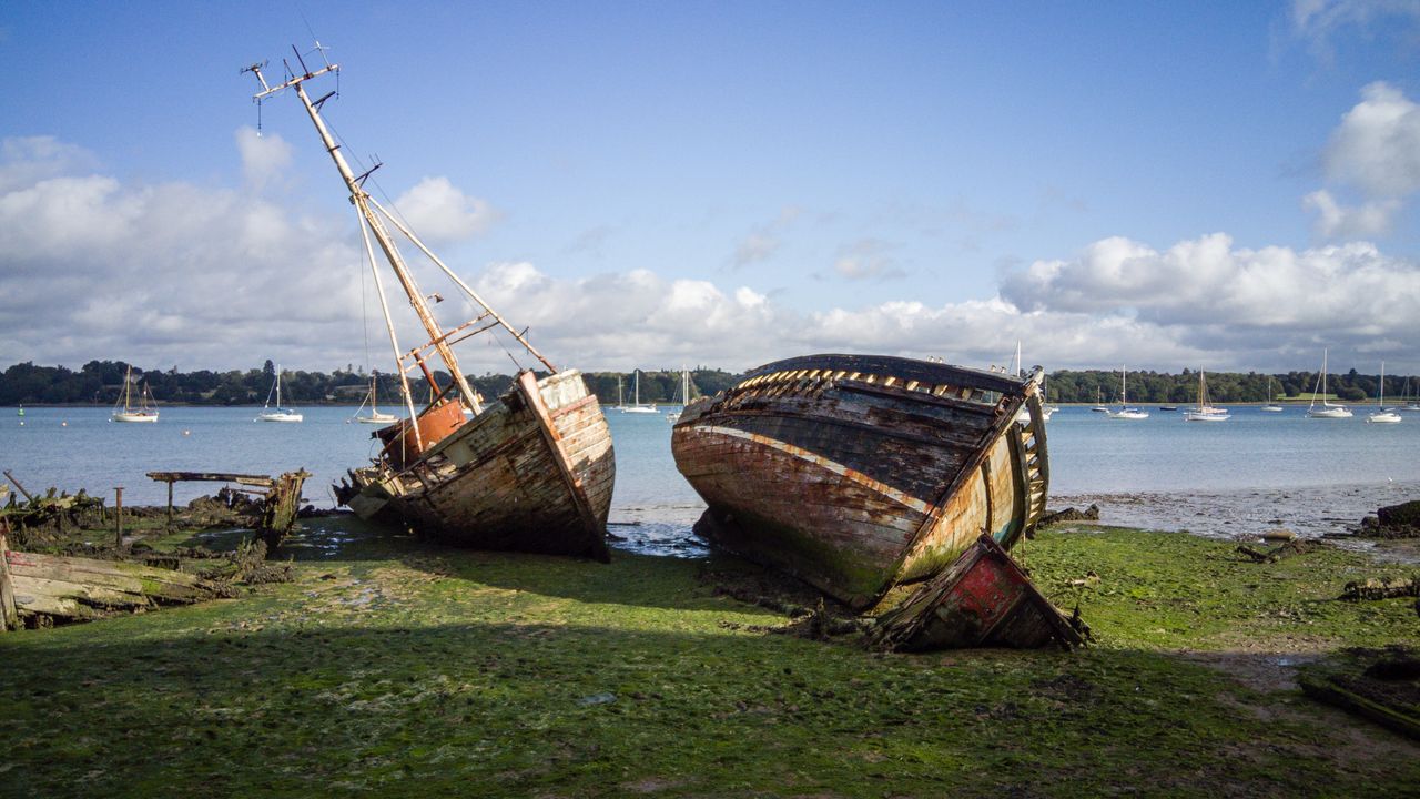 two boats laying on the grass near water.