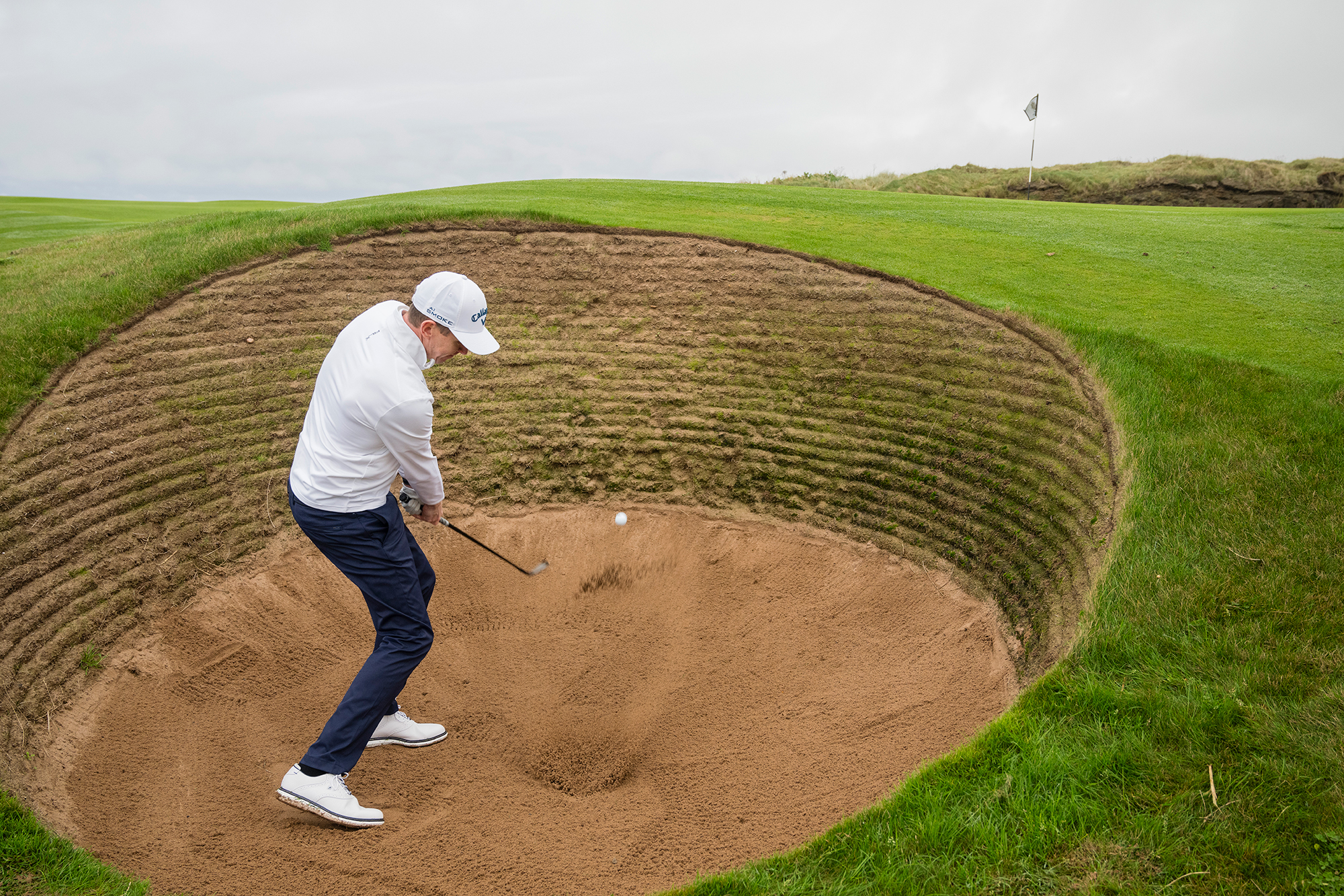 Ben Emerson just past impact after splashing the golf ball out of a deep revetted bunker at Trump Turnberry