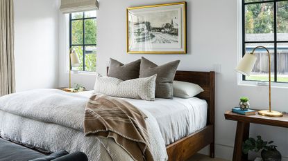 Bedroom with white walls and window, wood framed bed and white sheets, throw pillows and blankets