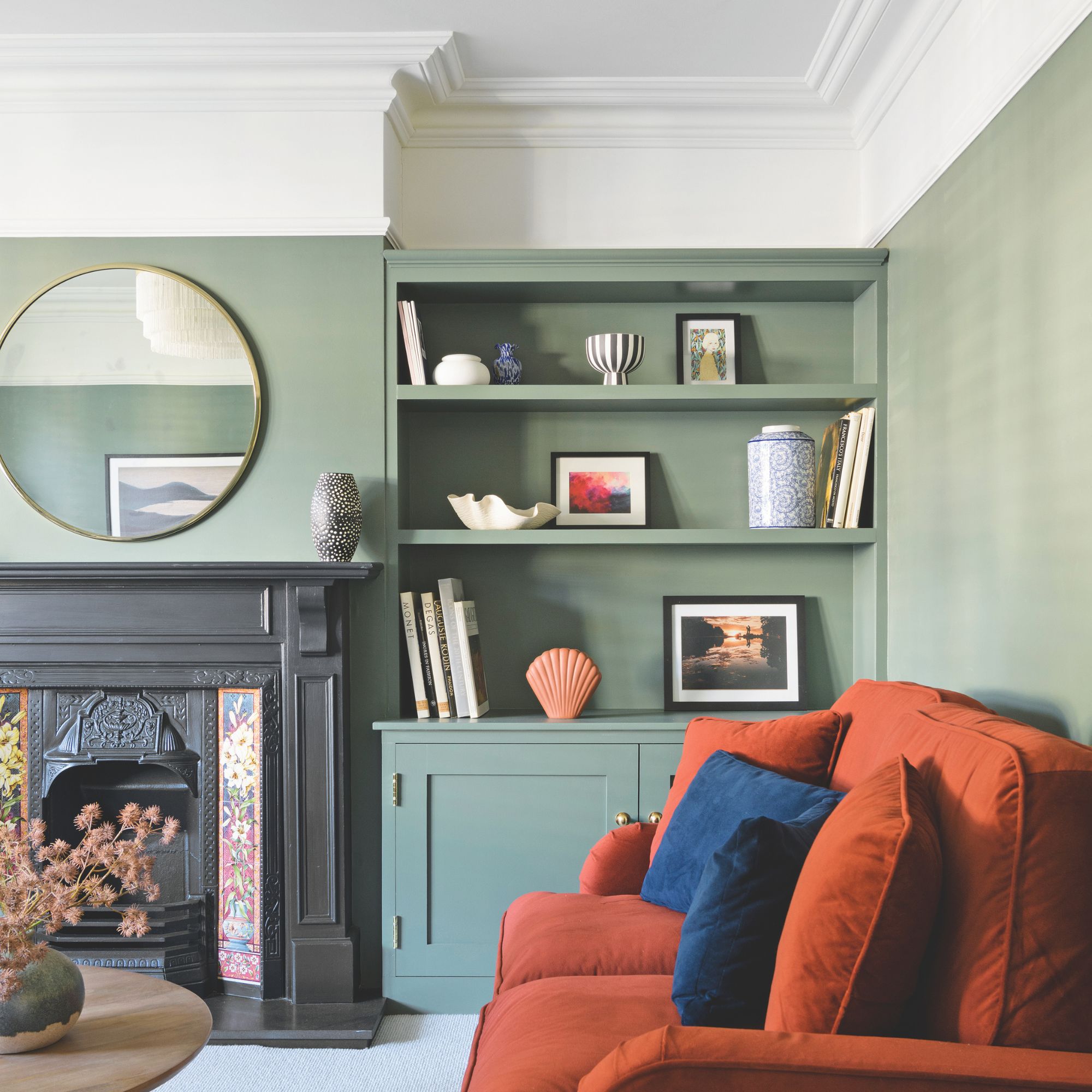 Sala de estar verde con estantes en la pared y tallas blancas, con un sofá naranja con cojines azules