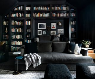 media room with black walls and dark gray sofa and fitted bookshelves
