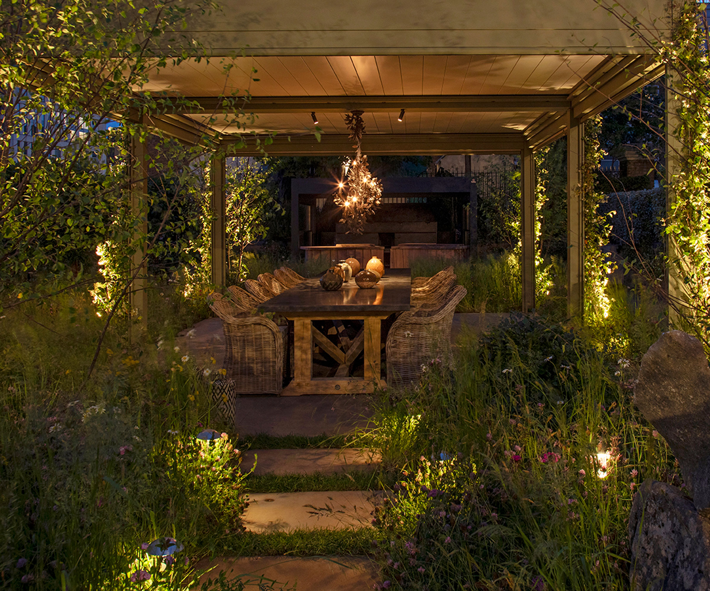 patio with garden furniture and tabletop lights, garden path illuminated by spike lights, pergola with climbing plants and lantern