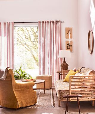 A summer living room with woven furniture, pink walls and pink striped drapes.