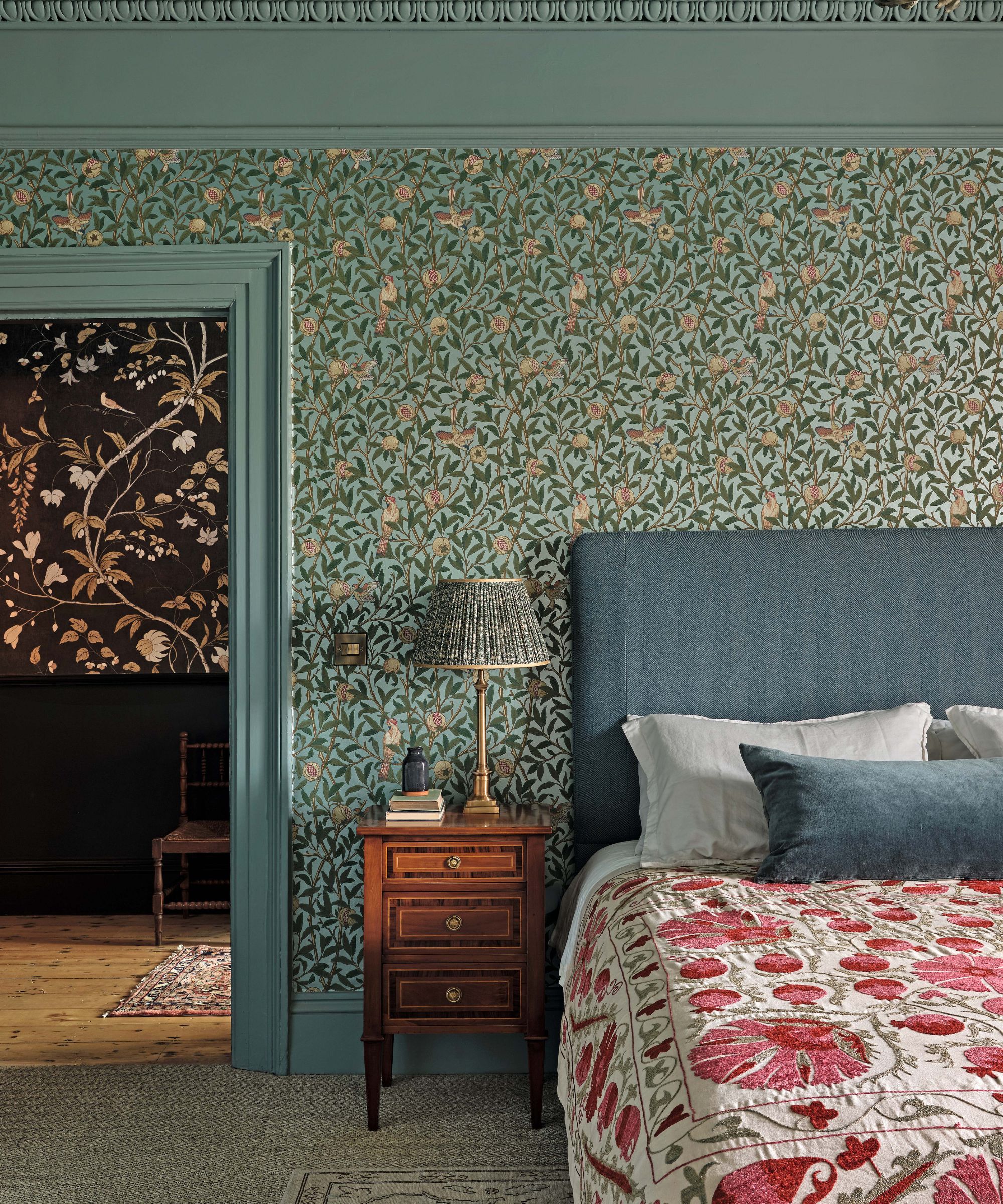 a blue floral wallpapered bedroom with painted molding and trims, blue headboard, and a suzani bed spread