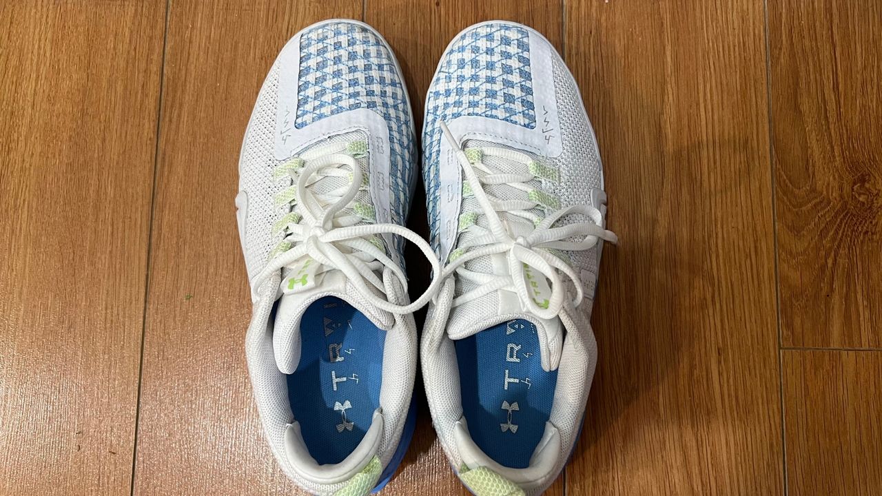 A pair of Under Armour Reign 6 on a wood floor shot topdown