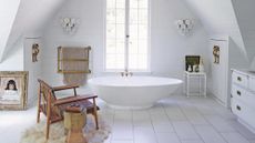 All white bathroom with stand alone tub. A wooden, antique chair sits by the tub on a furry rug