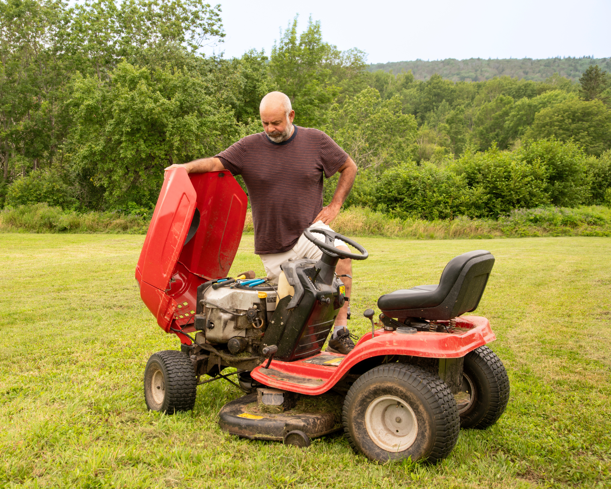 man looking under hood of riding mower