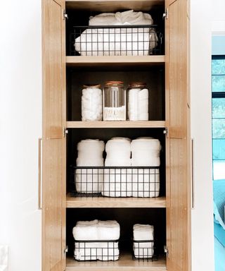 A bathroom cabinet with black wire baskets filled with towels