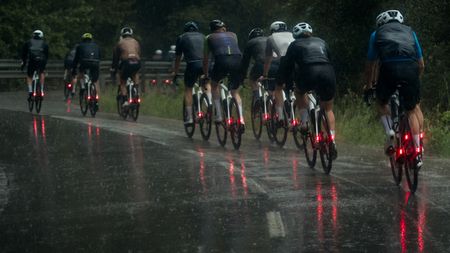 A group of cyclists cycling on a wet road in winter, each of them using winter road bike tyres and with bright red lights on the rear of their bikes