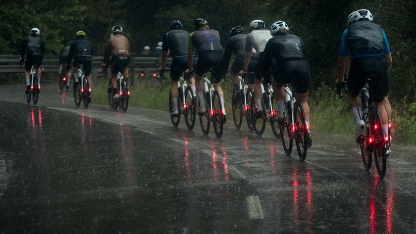 A group of cyclists cycling on a wet road in winter, each of them using a set of the best winter road bike tyres and with bright red lights on the rear of their bikes