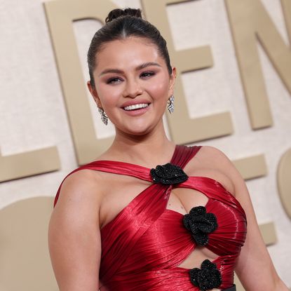 selena gomez smiles in a red dress with black flowers on the 2024 golden globes red carpet