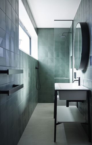 small teal bathroom with wall to ceiling tiles, white basin, glass doors, black fixtures and fittings