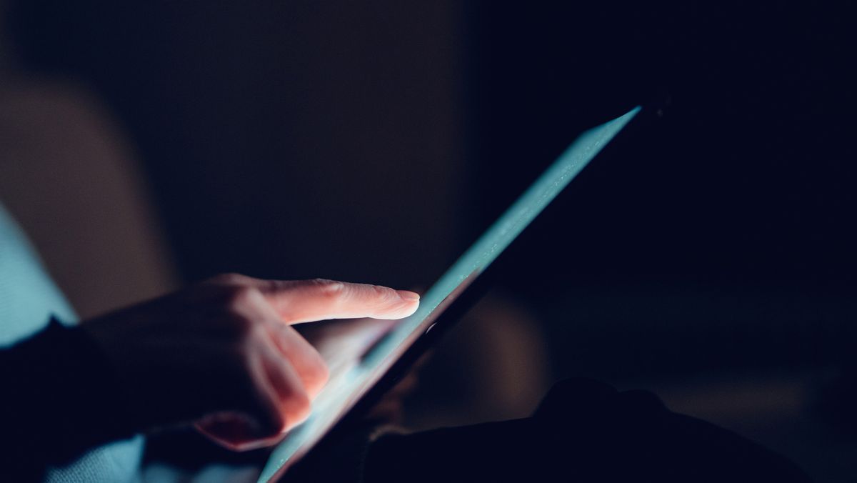 A woman&#039;s hand using a tablet, to represent women in tech. Decorative: the background is dark.