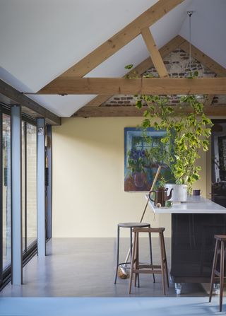 Open plan kitchen painted in Farrow and Ball Hay with kitchen island and white countertop, bar stools, artwork